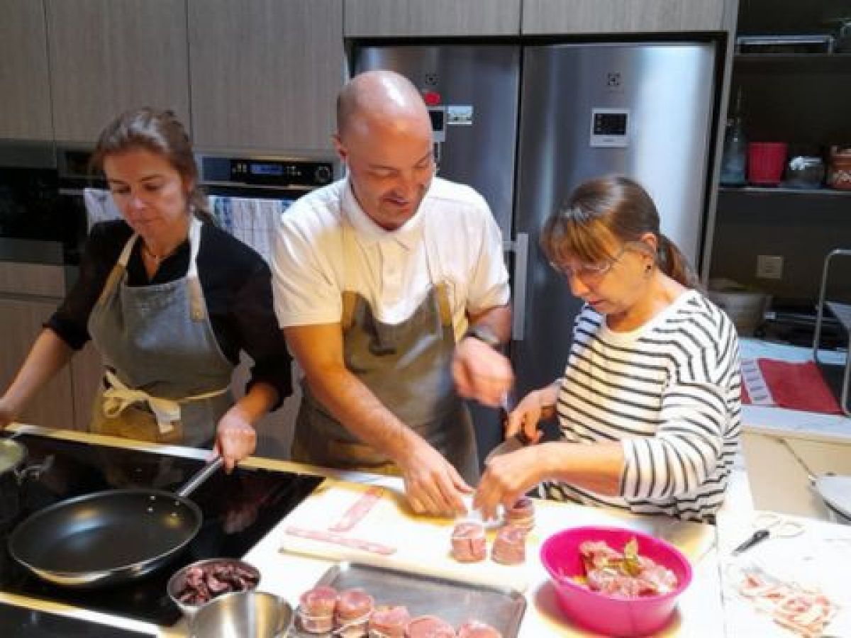 Two Portuguese chefs guide a group in a vibrant kitchen, sharing culinary skills during a vacation in Portugal.