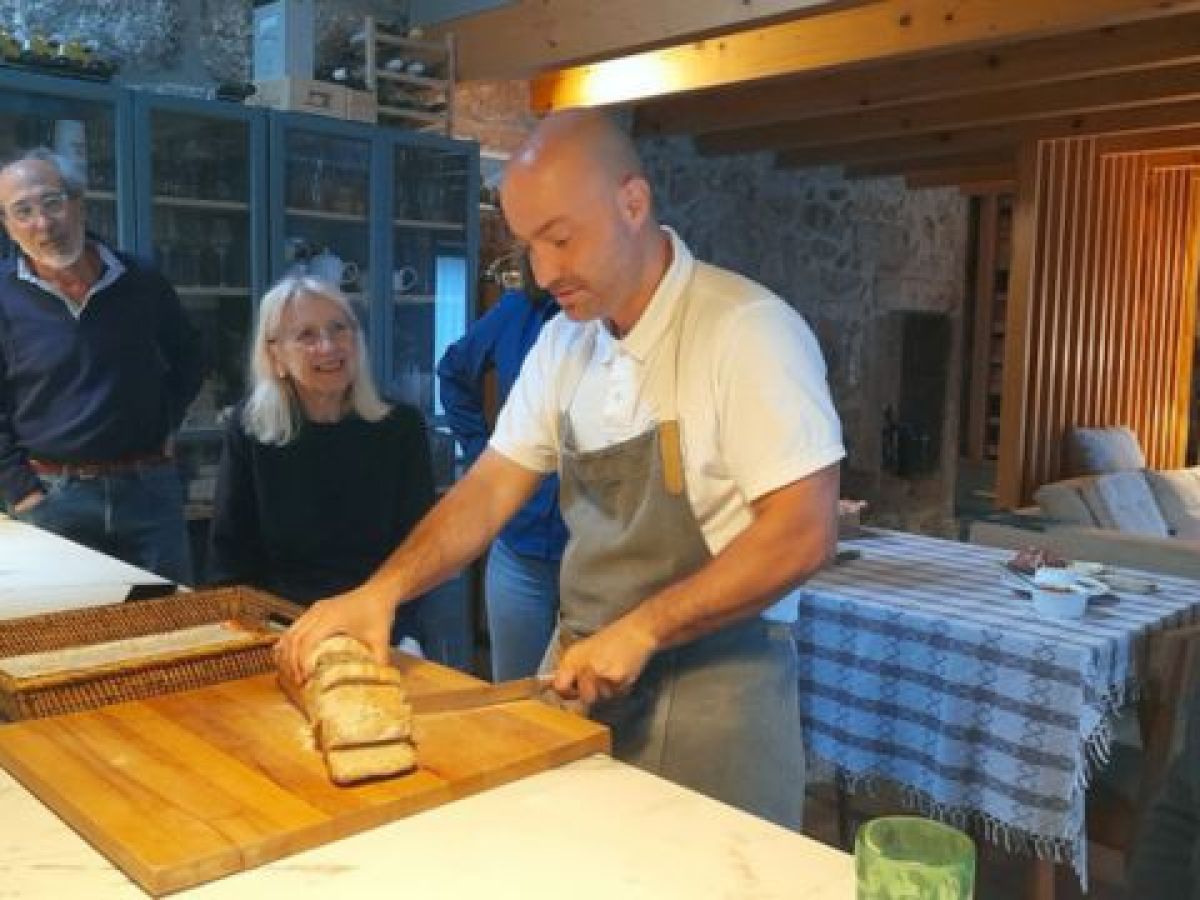The Portuguese Chef slices fresh bread in a cozy kitchen while eager guests watch, enjoying a culinary experience in Portugal.