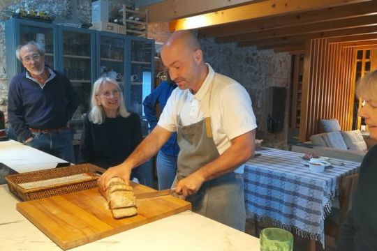 The Portuguese Chef slices fresh bread in a cozy kitchen while eager guests watch, enjoying a culinary experience in Portugal.