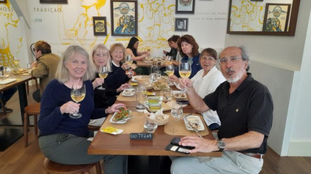 A small group of friends savoring Portuguese wine and sardines around a table, enjoying their vacation together.