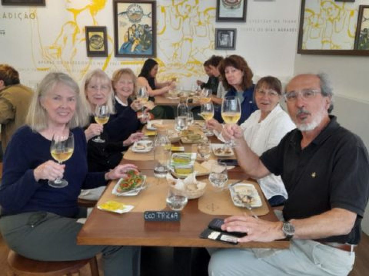 A small group of friends savoring Portuguese wine and sardines around a table, enjoying their vacation together.