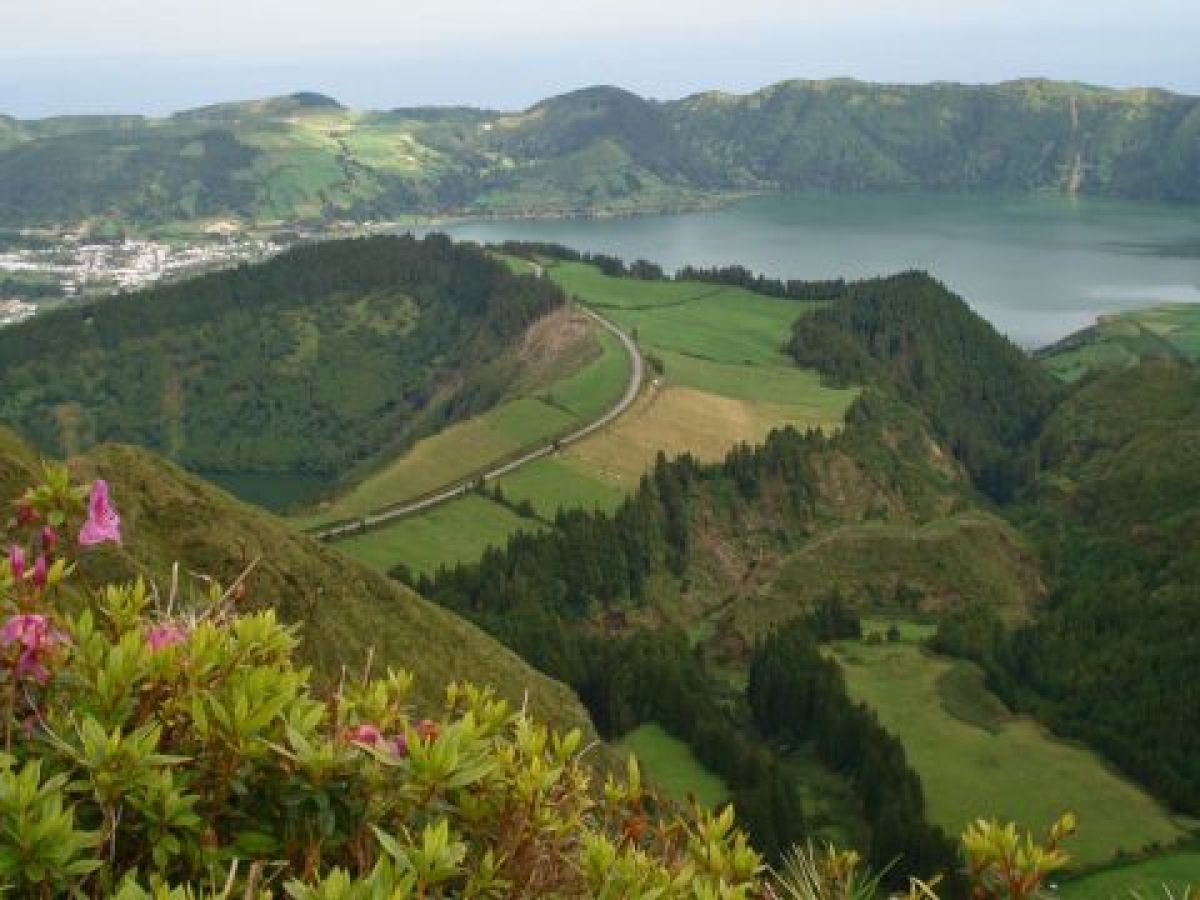 Scenic view of a lush valley and serene lake from a hilltop, showcasing the beauty of Azores nature tours in small groups.