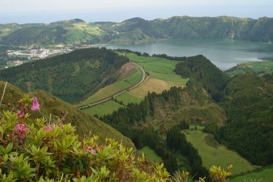Scenic view of a lush valley and serene lake from a hilltop, showcasing the beauty of Azores nature tours in small groups.