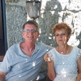 Two people sitting outside on a sunny day, smiling at the camera.