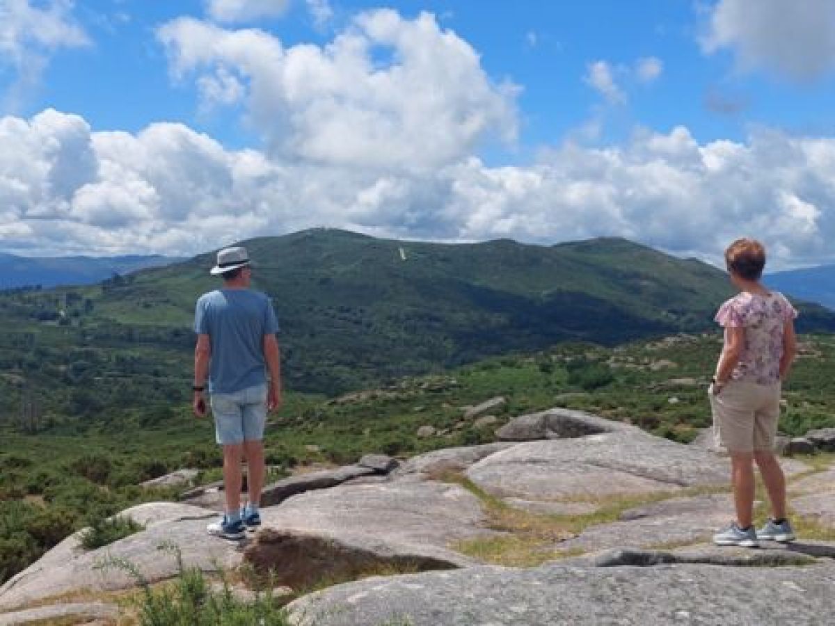 Two hikers stand triumphantly on a mountain peak, overlooking the stunning scenic countryside of Portugal.