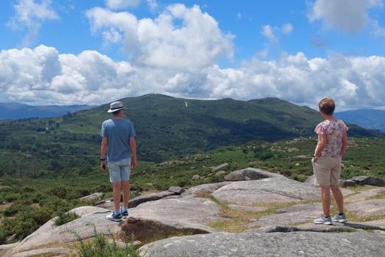 Two hikers stand triumphantly on a mountain peak, overlooking the stunning scenic countryside of Portugal.