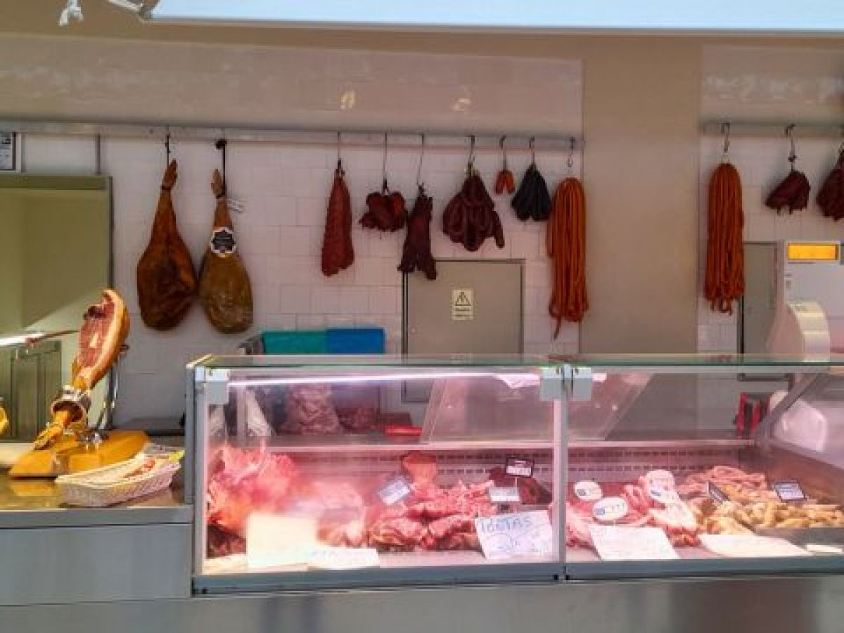 A butcher's counter displaying an array of meats hanging on the wall, showcasing the rich offerings of a farm market tour in Porto