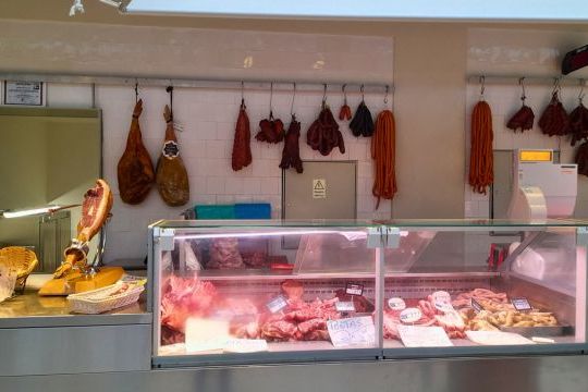 A butcher's counter displaying an array of meats hanging on the wall, showcasing the rich offerings of a farm market tour in Porto