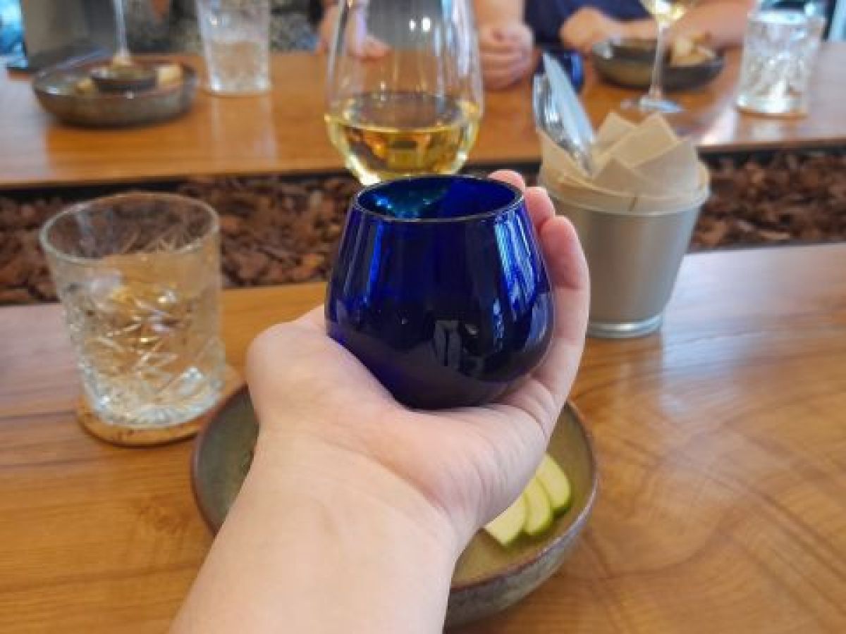 A hand grips a blue glass, ready for an olive oil tasting, blending the art of tasting with a touch of sophistication.