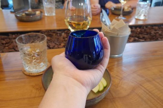 A hand grips a blue glass, ready for an olive oil tasting, blending the art of tasting with a touch of sophistication.