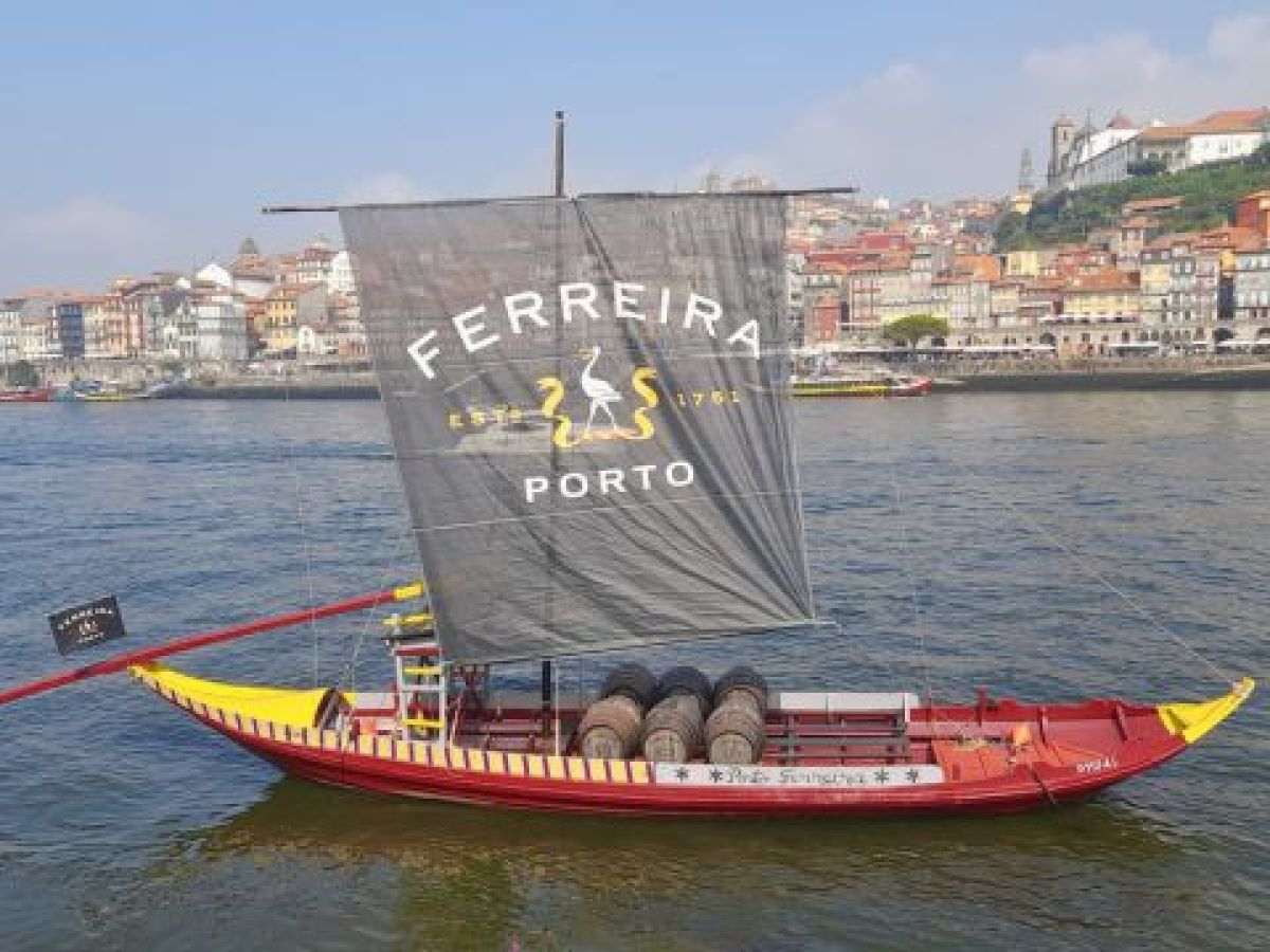 A sailboat glide on the Douro River, with the vibrant city of Porto in the background, showcasing a scenic tour experience.