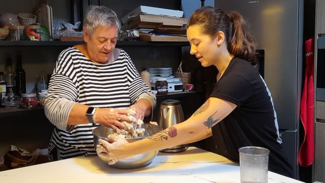 A woman and an older woman joyfully prepare traditional Portuguese bread in a cozy kitchen during a cooking vacation in Portugal.