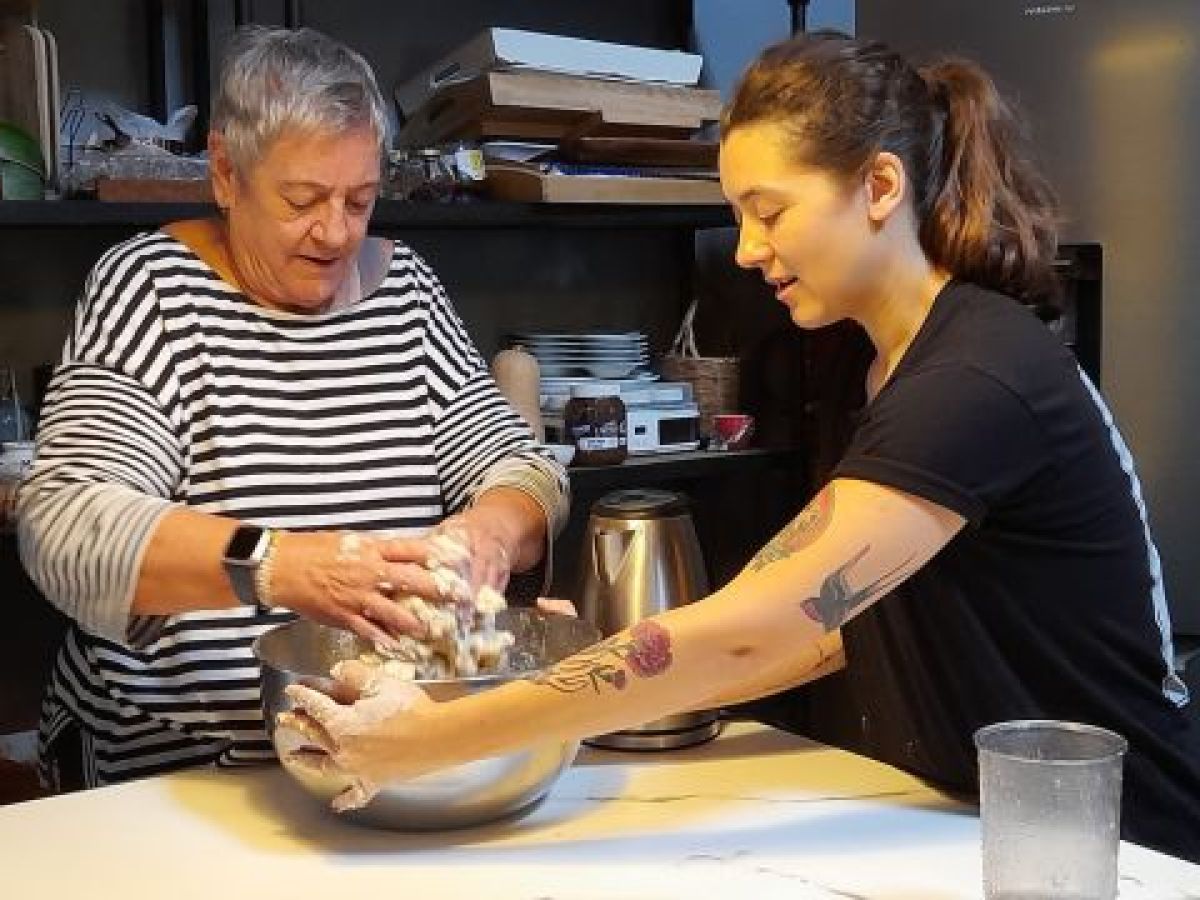 A woman and an older woman joyfully prepare traditional Portuguese bread in a cozy kitchen during a cooking vacation in Portugal.