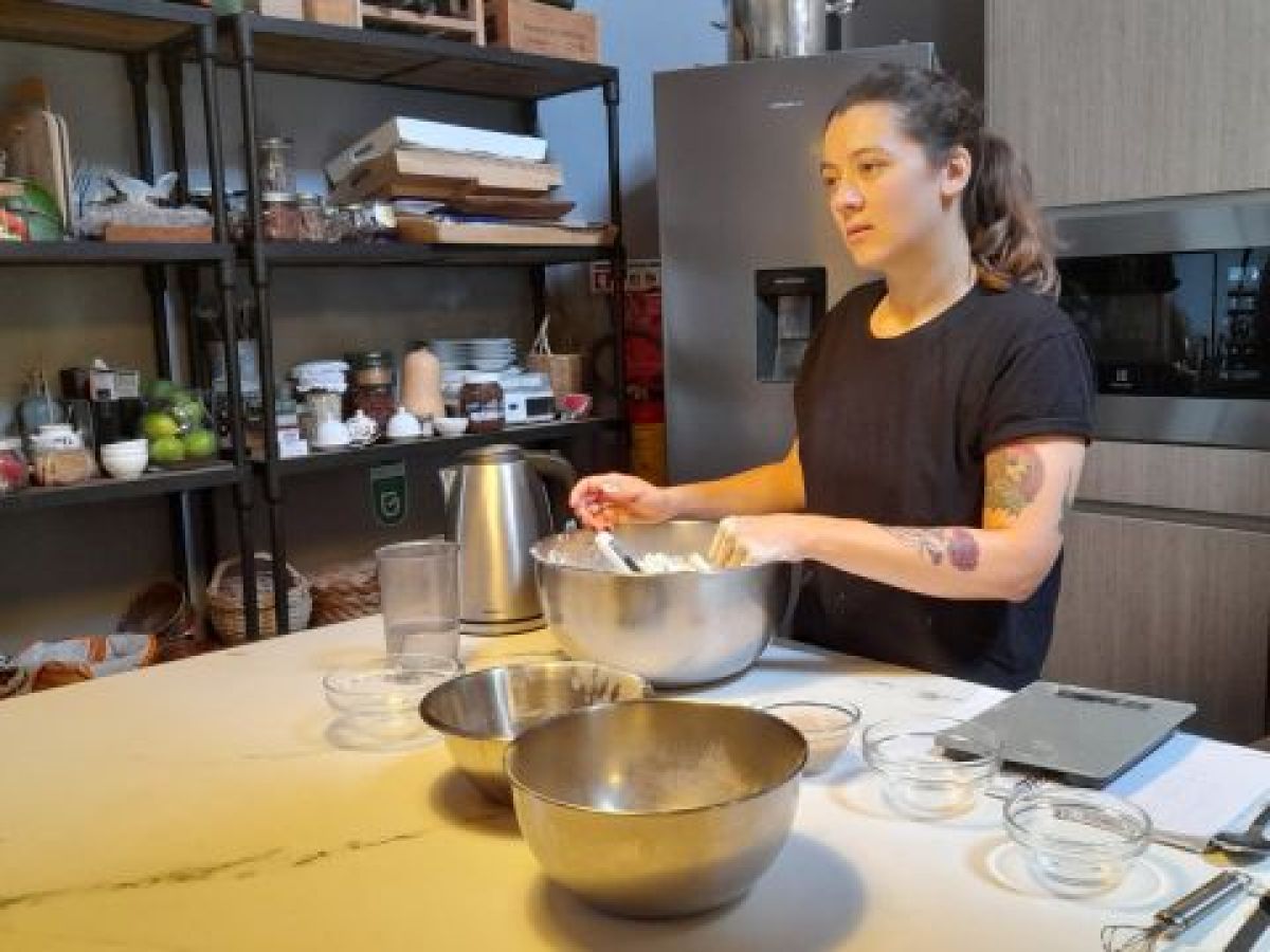A woman joyfully mixes ingredients in a kitchen, preparing for a delicious Portuguese bread during a cooking vacation.