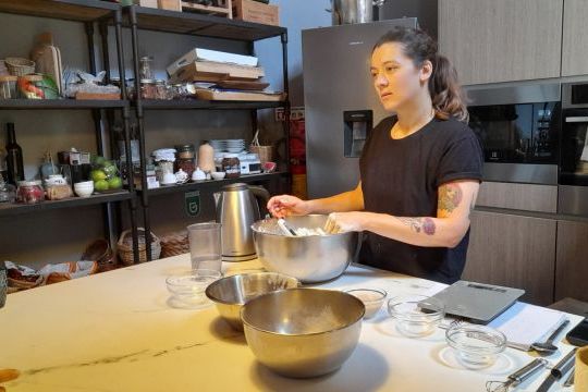 A woman joyfully mixes ingredients in a kitchen, preparing for a delicious Portuguese bread during a cooking vacation.