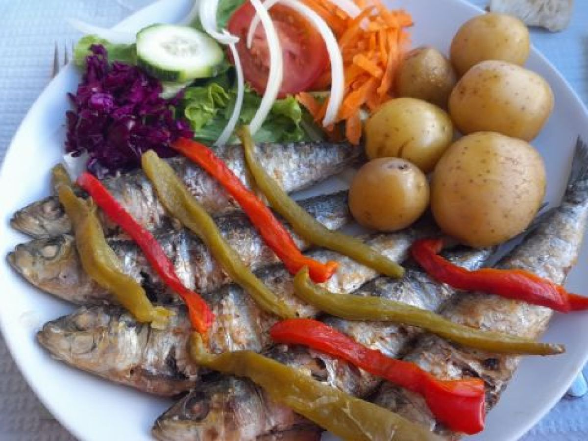 A tempting dish of sardines, potatoes, and assorted vegetables on a table, showcasing the flavors of a culinary vacation in Portugal