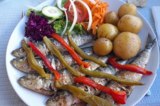 A tempting dish of sardines, potatoes, and assorted vegetables on a table, showcasing the flavors of a culinary vacation in Portugal