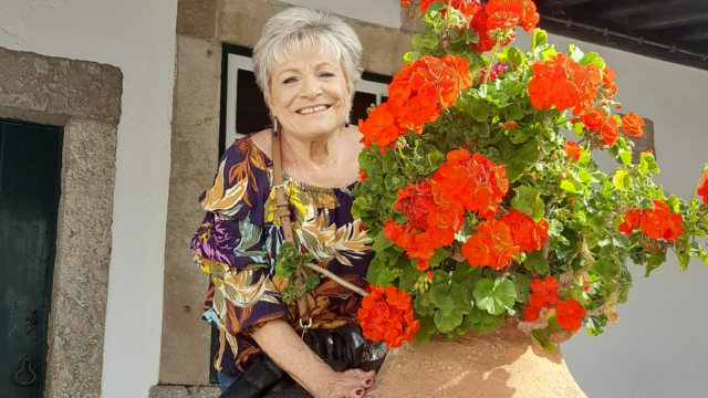 An older woman smiles as she holds a large pot of blooming flowers, enjoying springtime in Portugal during a small group tour.