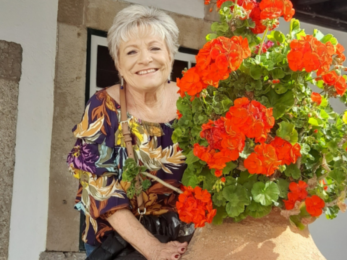 An older woman smiles as she holds a large pot of blooming flowers, enjoying springtime in Portugal during a small group tour.