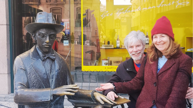 A couple stands by a statue, discovering Lisbon's local cafes during a delightful walking tour with a guide.