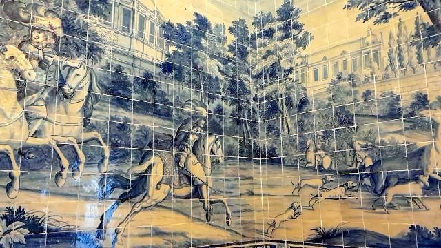 A mural depicting horses and people in a palace, complemented by Portuguese tiles appreciated by a small tour group.