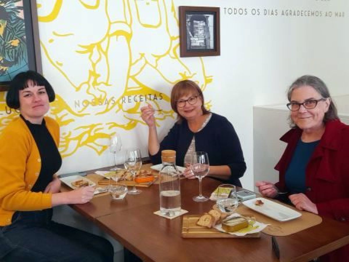 Three women enjoying a meal at a table in Porto, Portugal, celebrating their solo travel experience together.