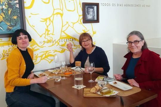 Three women enjoying a meal at a table in Porto, Portugal, celebrating their solo travel experience together.