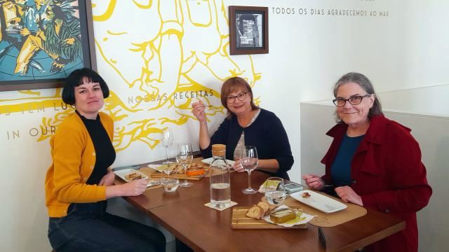Three women enjoying a meal at a table in Porto, Portugal, celebrating their solo travel experience together.