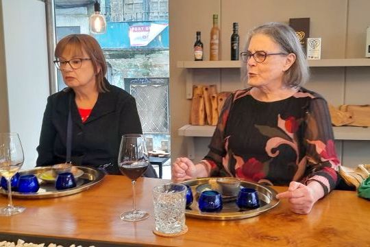 Two women at a table in Porto, Portugal, sipping wine and participating in an olive oil tasting.