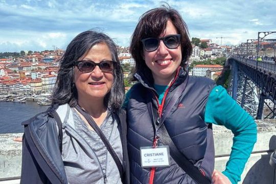 Guide Cris Fonte and a guest pose on a bridge in Porto, with the vibrant cityscape behind them during a walking tour.