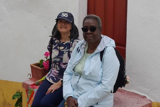 Two women sit on steps outside a house in Obidos, enjoying a small group tour in the charming medieval village of Portugal.