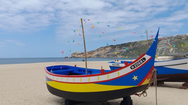 Vibrant boats parked on the beautiful Nazare beach in Portugal, surrounded by soft sand and a clear blue sky.