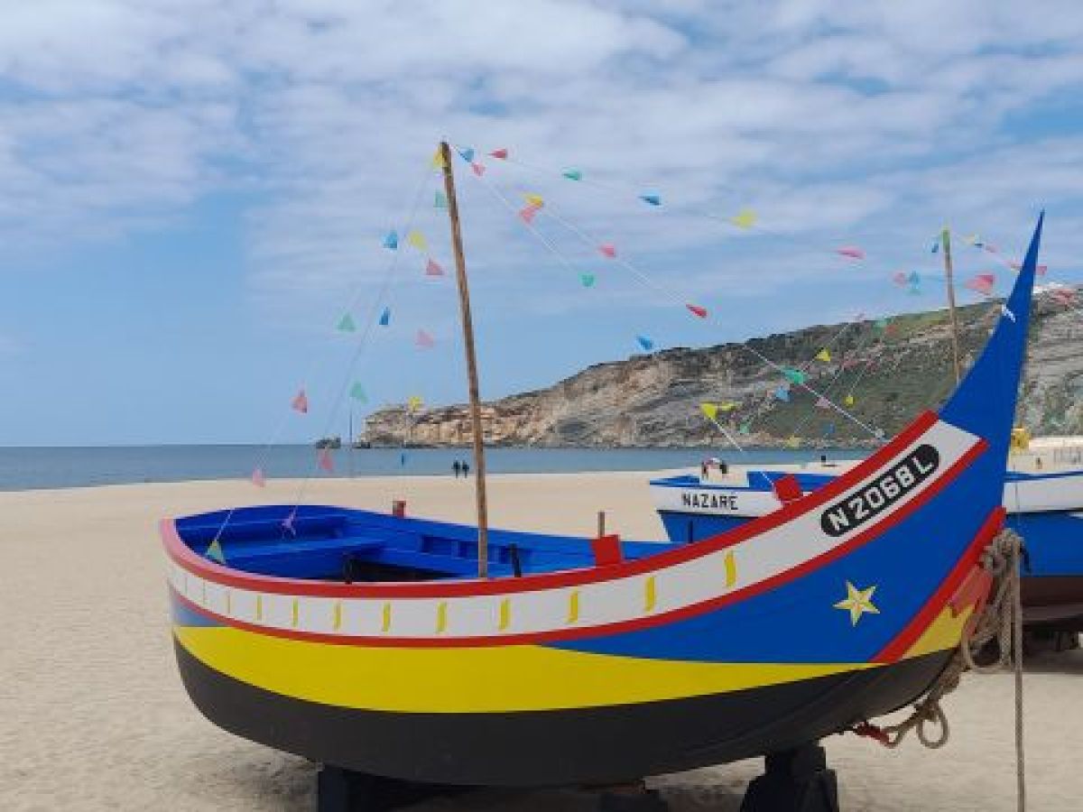 Vibrant boats parked on the beautiful Nazare beach in Portugal, surrounded by soft sand and a clear blue sky.