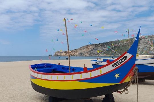 Vibrant boats parked on the beautiful Nazare beach in Portugal, surrounded by soft sand and a clear blue sky.