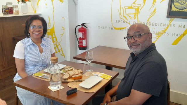 A couple sits at a table, tasting sardines after visiting a sardine factory cannery, surrounded by delicious food.