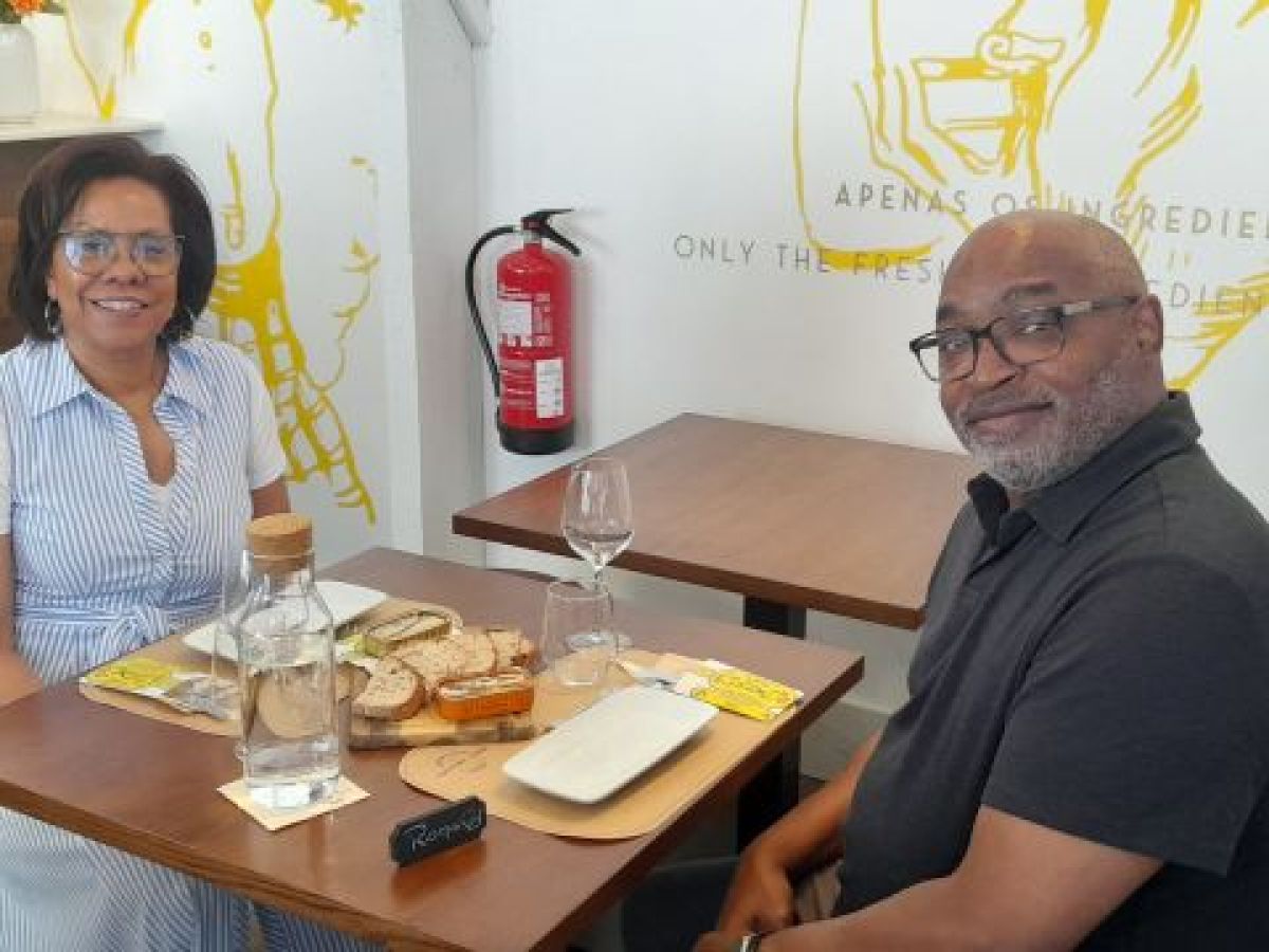 A couple sits at a table, tasting sardines after visiting a sardine factory cannery, surrounded by delicious food.