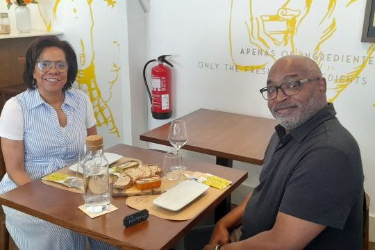 A couple sits at a table, tasting sardines after visiting a sardine factory cannery, surrounded by delicious food.