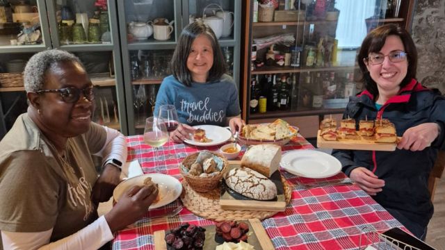 A small group of three women sits at a table, sharing and enjoying traditional Portuguese food after their cooking class.