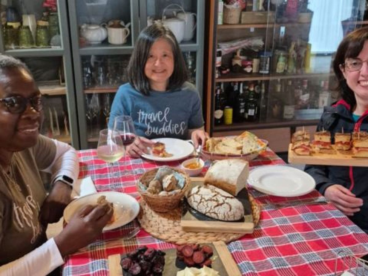 A small group of three women sits at a table, sharing and enjoying traditional Portuguese food after their cooking class.