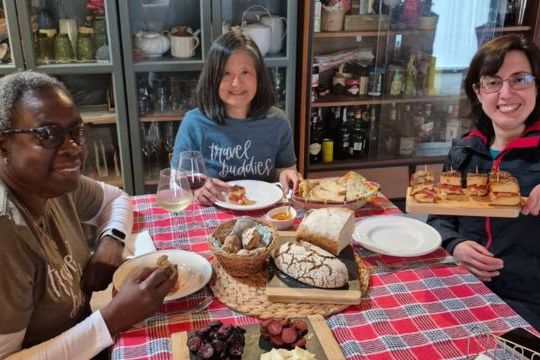A small group of three women sits at a table, sharing and enjoying traditional Portuguese food after their cooking class.