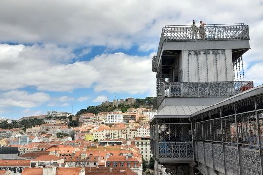A panoramic view of Lisbon from the top of Elevador Santa Justa, showcasing the city's rooftops and historic architecture.