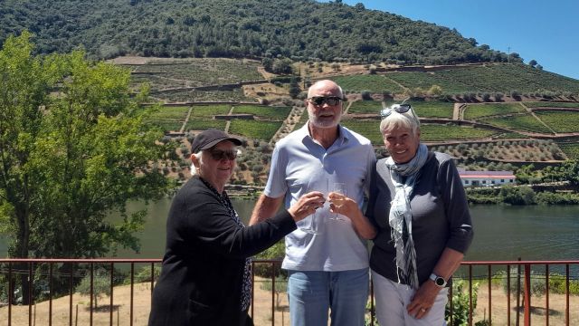 A small group enjoys wine by a river, with lush vineyards of the Douro Valley visible behind them.