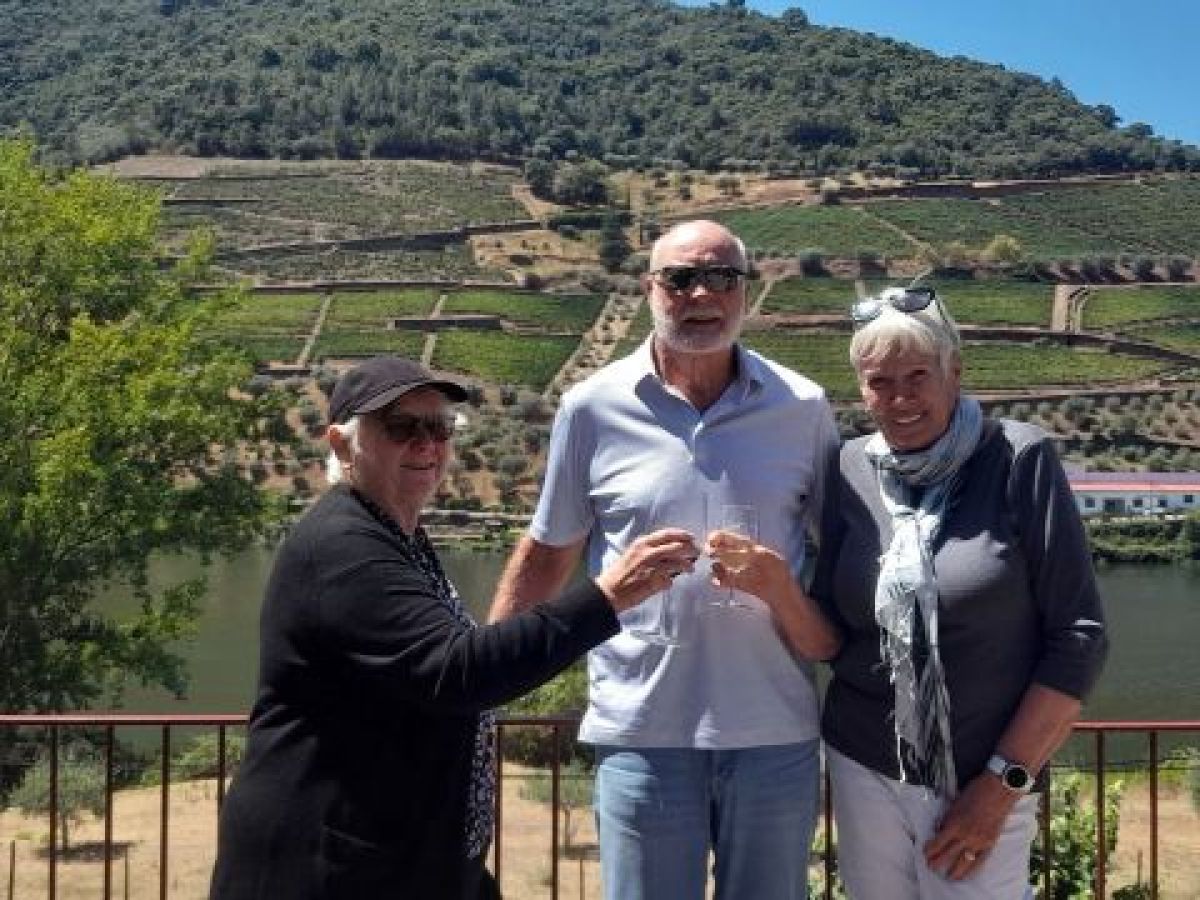 A small group enjoys wine by a river, with lush vineyards of the Douro Valley visible behind them.