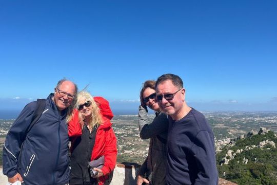 A group of four stands smiling in front of Pena Palace, captured during a private tour in Sintra, highlighting the Moors castle.