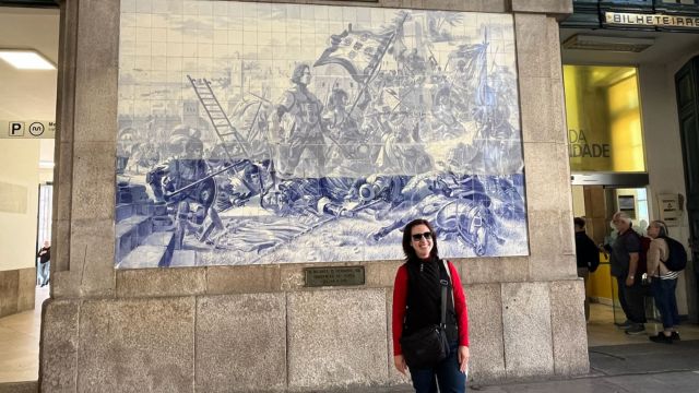 A tour guide woman poses in front of a large blue and white mural at São Bento train station in Porto.