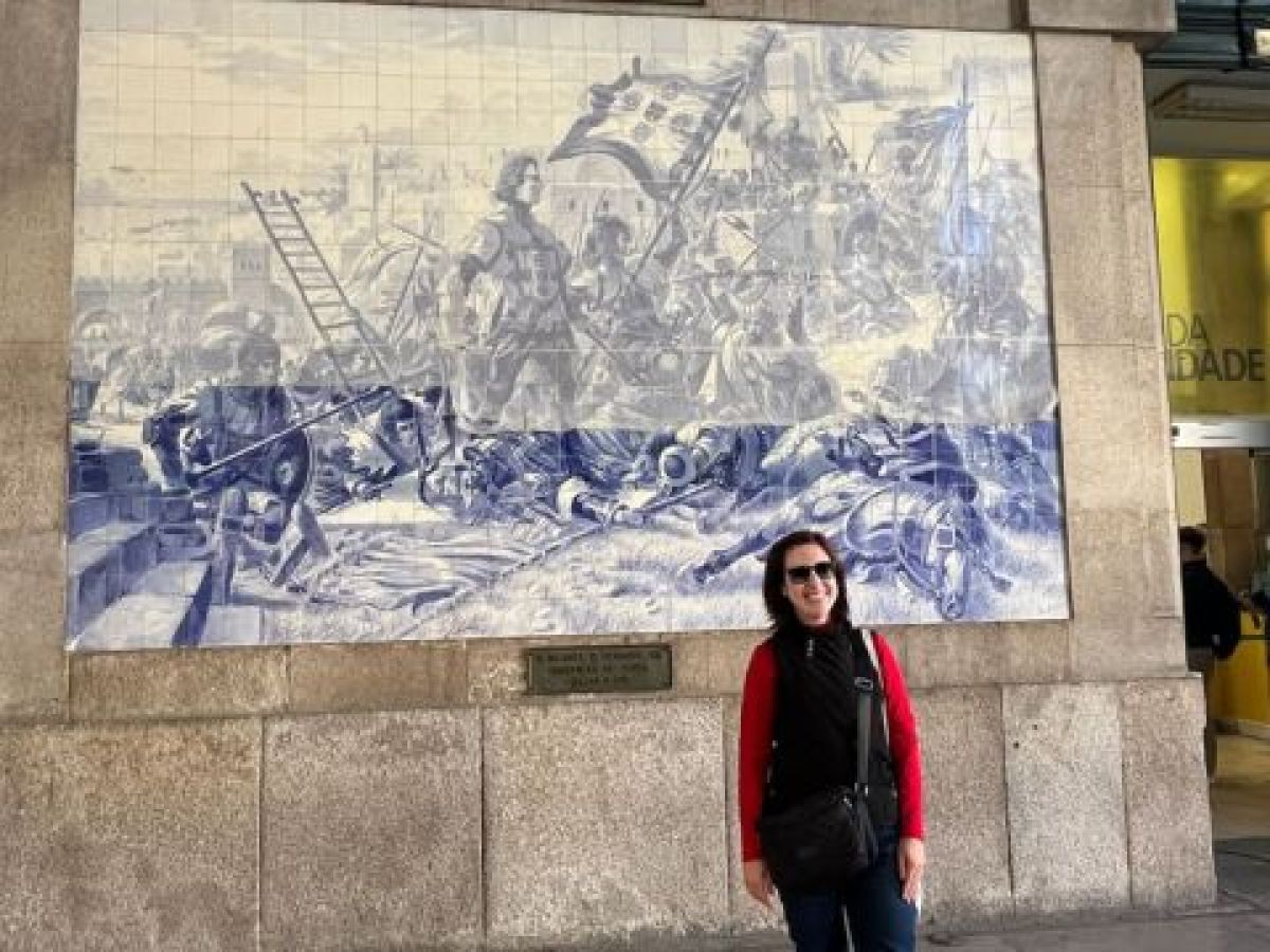 A tour guide woman poses in front of a large blue and white mural at São Bento train station in Porto.