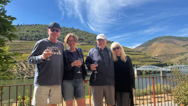 Two couples smile and pose with wine glasses during a private tour in the scenic Douro Valley.