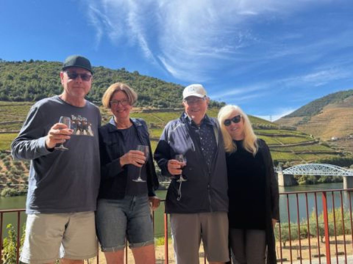 Two couples smile and pose with wine glasses during a private tour in the scenic Douro Valley.