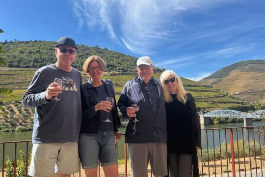 Two couples smile and pose with wine glasses during a private tour in the scenic Douro Valley.