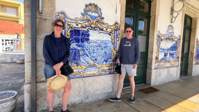 Two people stand before a building adorned with blue and white tiles during a private tour of the Douro Valley train station.